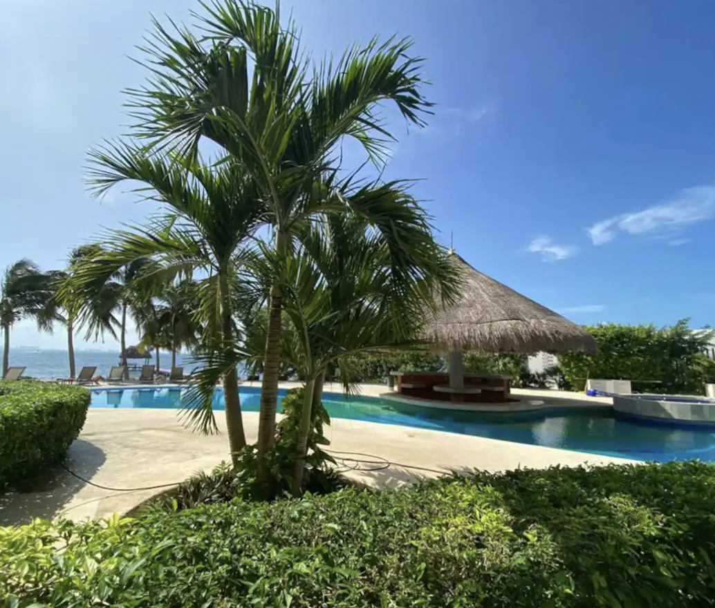 Pool ringed by palm trees with palapa bar and jacuzzi at the condo