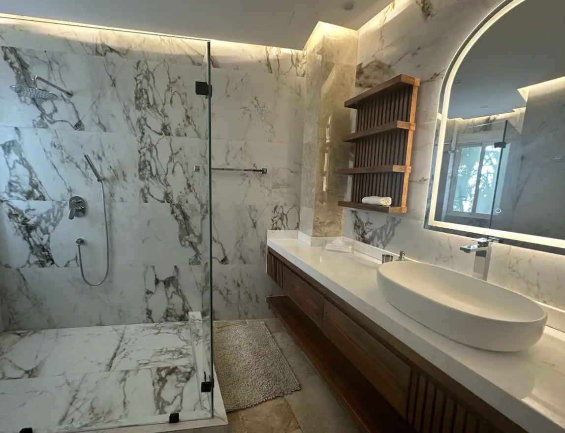 Bathroom with arched LED mirror, vessel sink and wood detailing in the vacation apartment