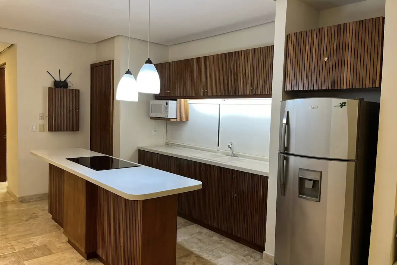 Equipped kitchen with central island, induction cooktop and wood cabinetry at Condominios Puerta al Mar