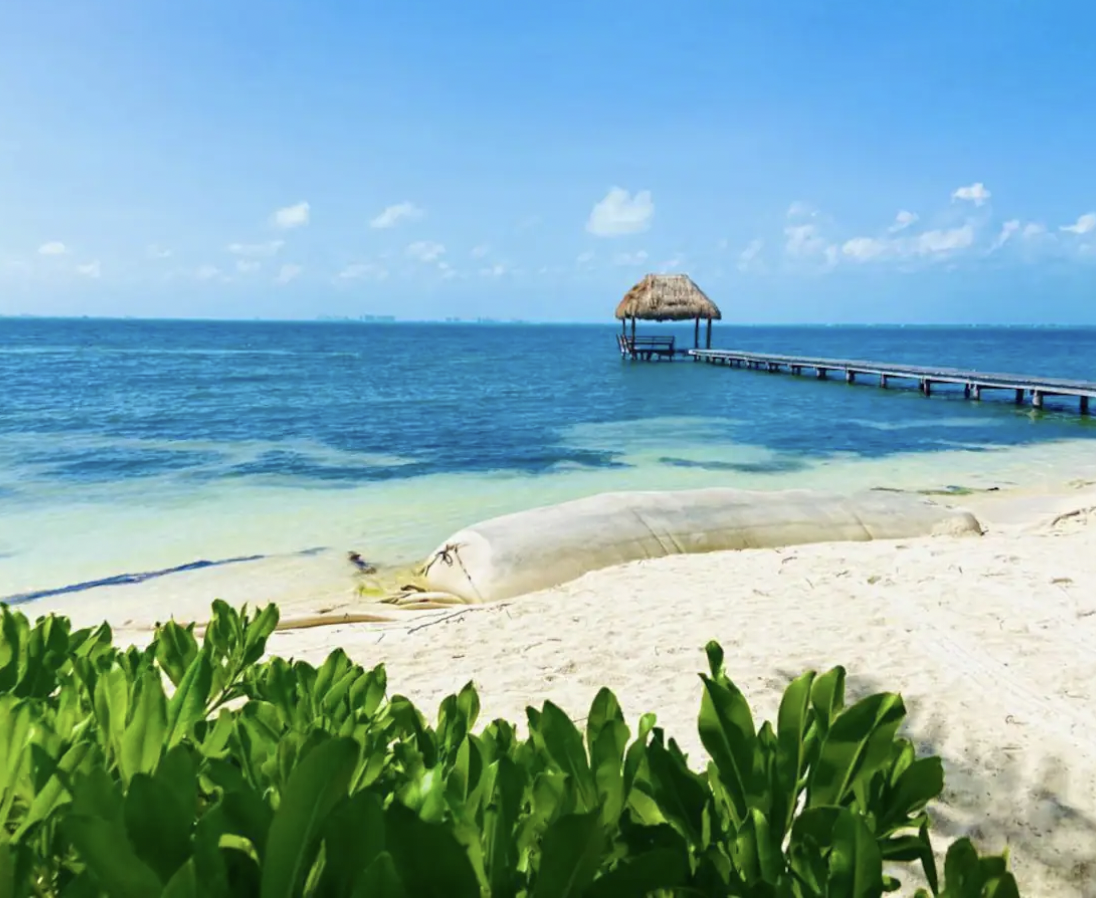 Private white-sand beach with palapa over a wooden pier in Isla Mujeres