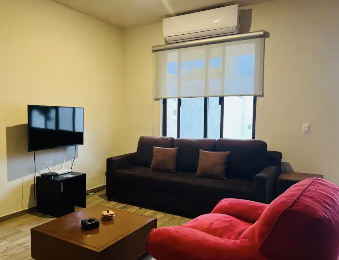 Living room with flat-screen TV, brown sofa, red armchair and A/C at Villa La Ceiba